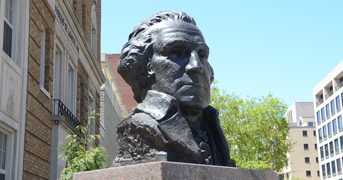 Bust of George Washington in front of green trees and campus buildings.